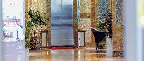 A hotel lobby with a reception desk, a coffee shop sign, and a modern elevator.
