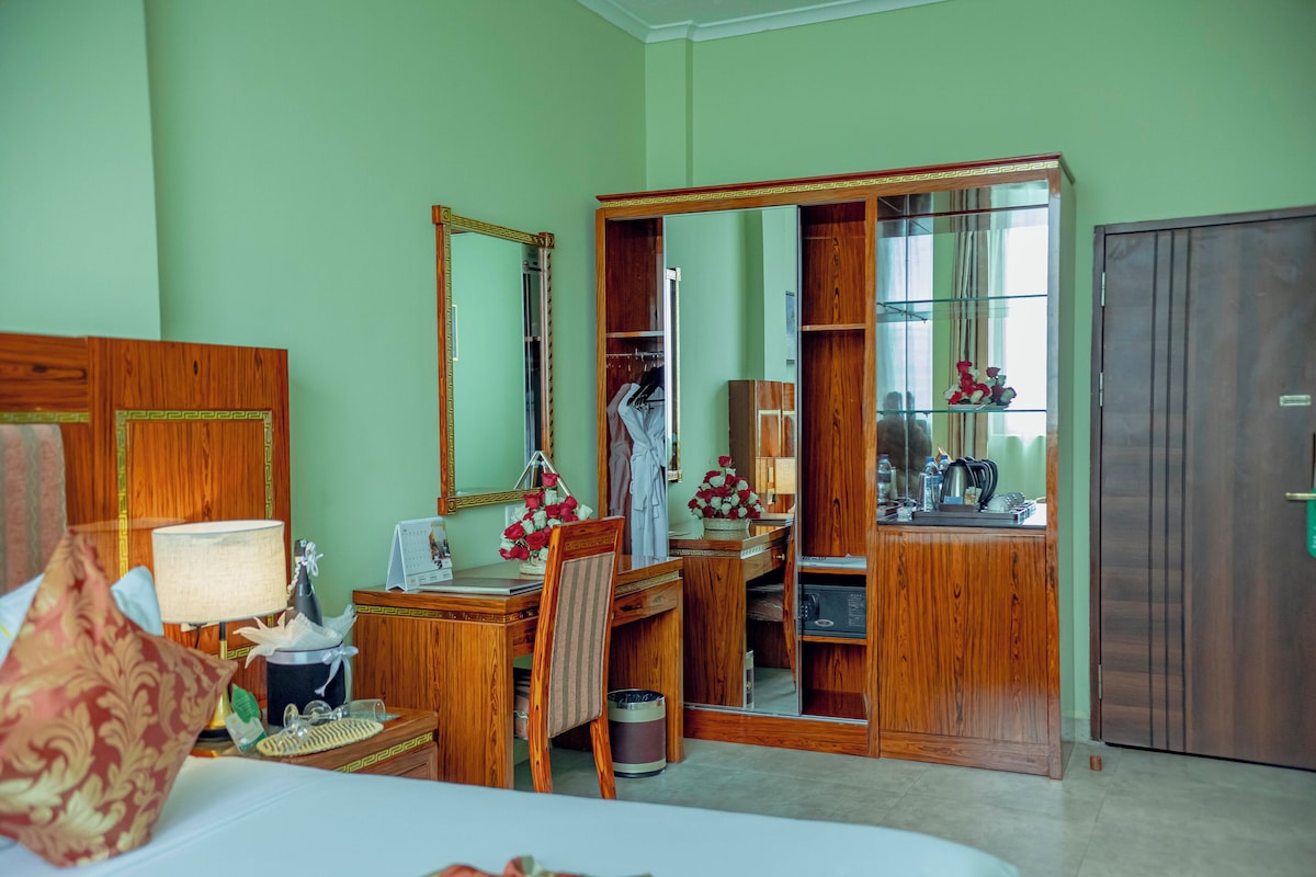 Habitació d'hotel amb llit, escriptori amb làmpada, cadira, armari, mirall i petit moble.