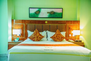 Una camera d'albergo con un letto, due lampade ai comodini, una televisione a parete e una testiera in legno.