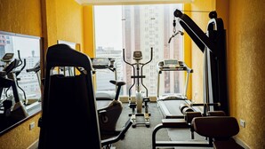 Ein Fitnessstudio mit Trainingsgeräten, Laufband und Fenster mit Blick auf die Stadt.