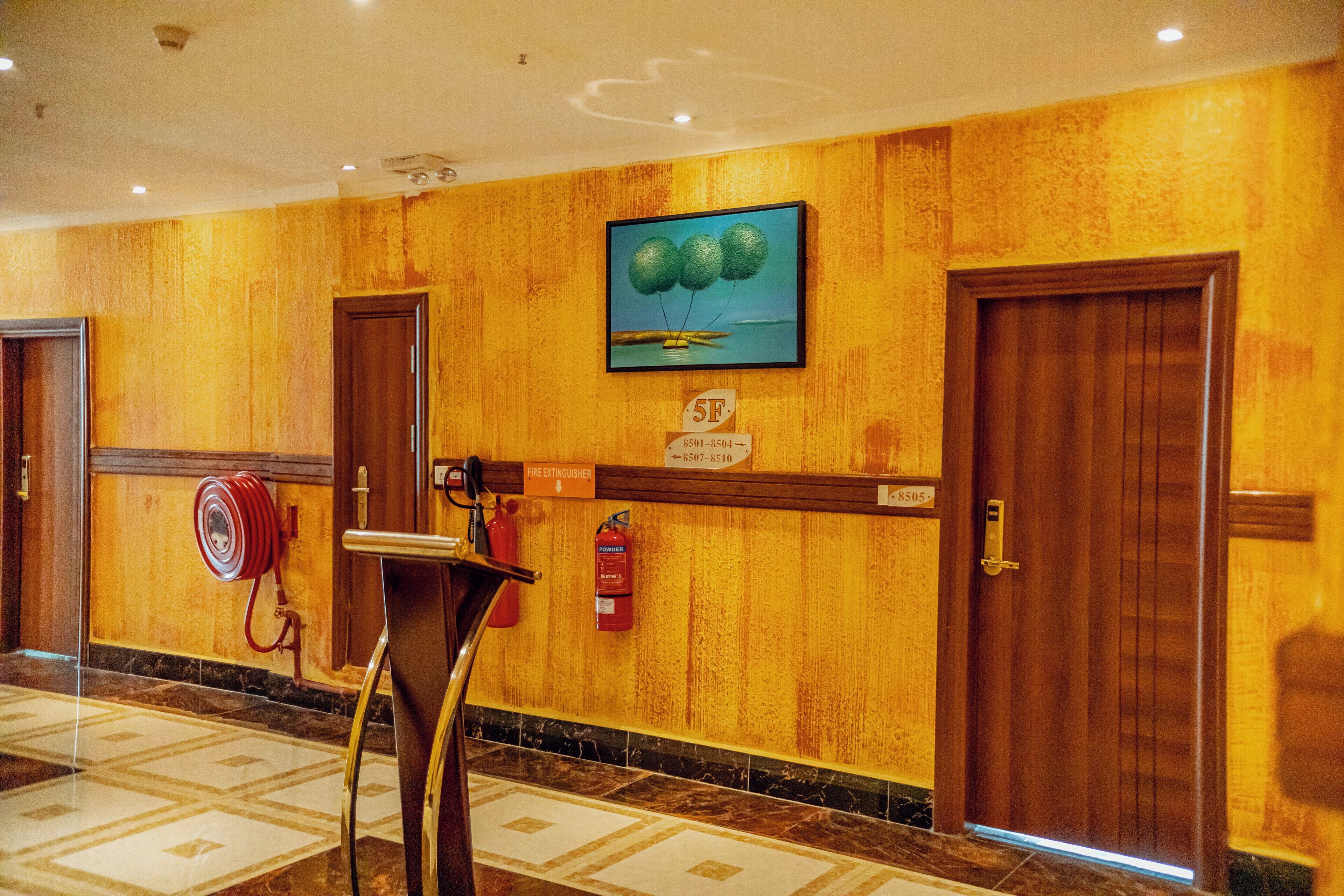 A hotel lobby with a fire extinguisher, a painting, and a fire alarm on the wall.