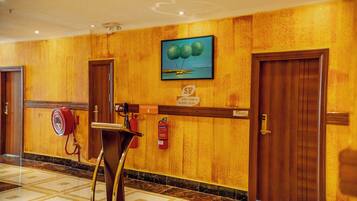 A hotel lobby with a fire extinguisher, a painting, and a fire alarm on the wall.