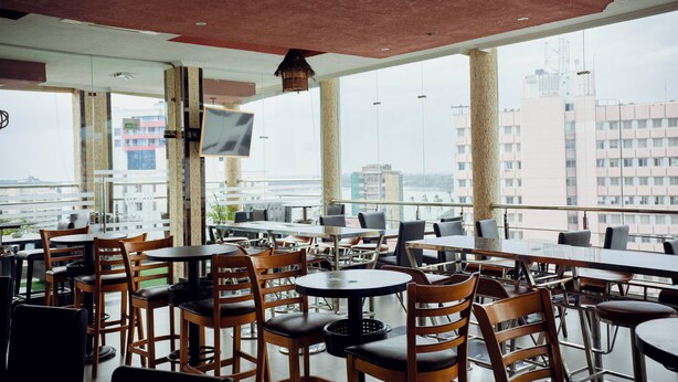 Ein Restaurant mit hohen Tischen und Stühlen, großen Fenstern und Blick auf die Stadt.