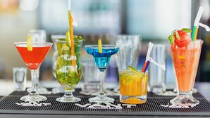 Verschiedene farbenfrohe Cocktails auf einer Bartischauflage vor unscharfem Hintergrund.