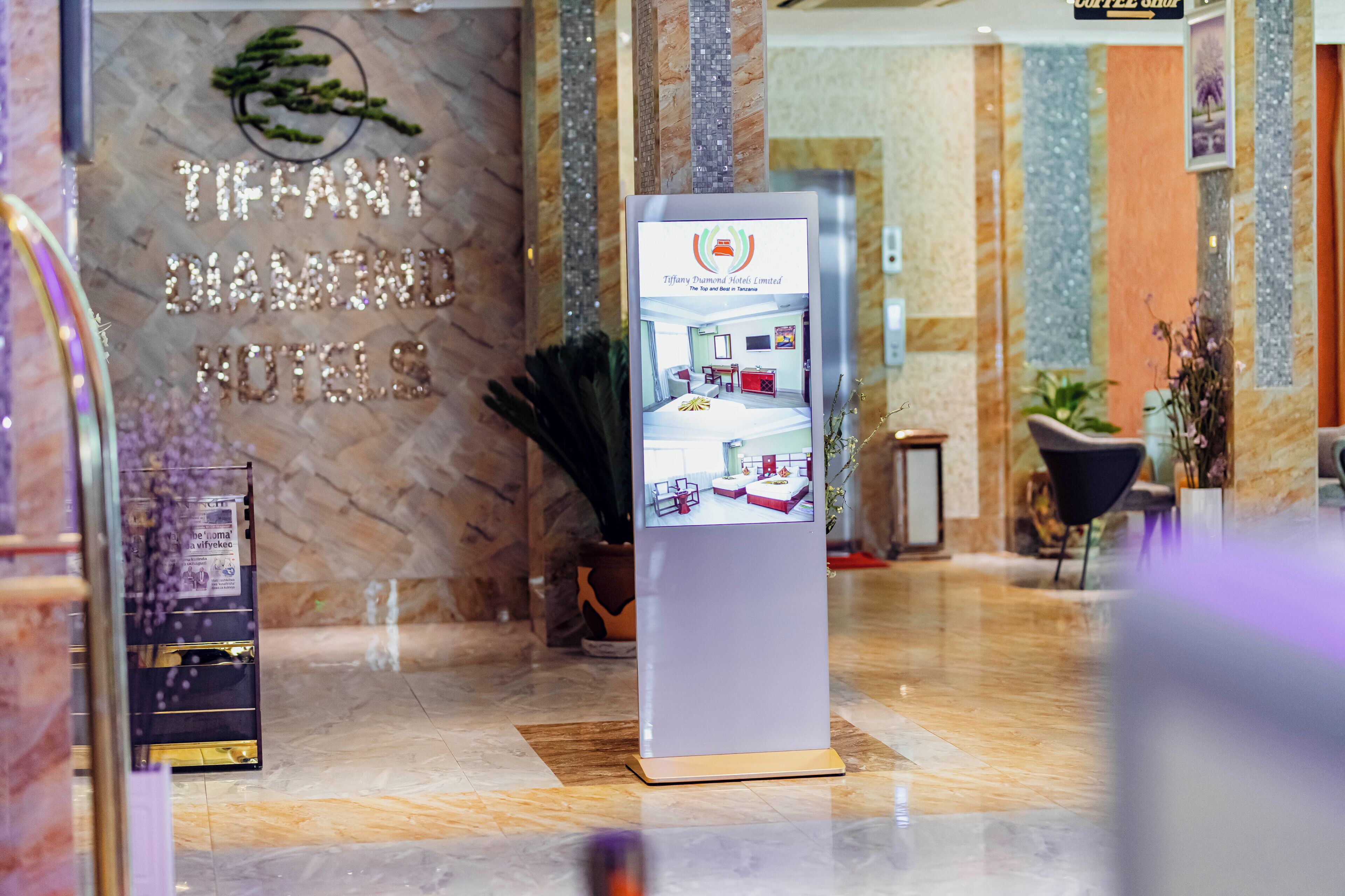 A hotel reception area with a marble wall, a reception desk, and a digital display.