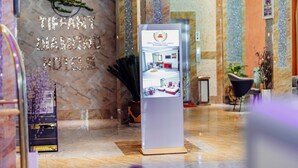 Een hotel receptie met een marmeren wand, een receptiebalie en een digitaal scherm.