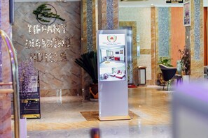 Un espace d’accueil d’hôtel avec un mur en marbre, un comptoir d’accueil et un écran numérique.