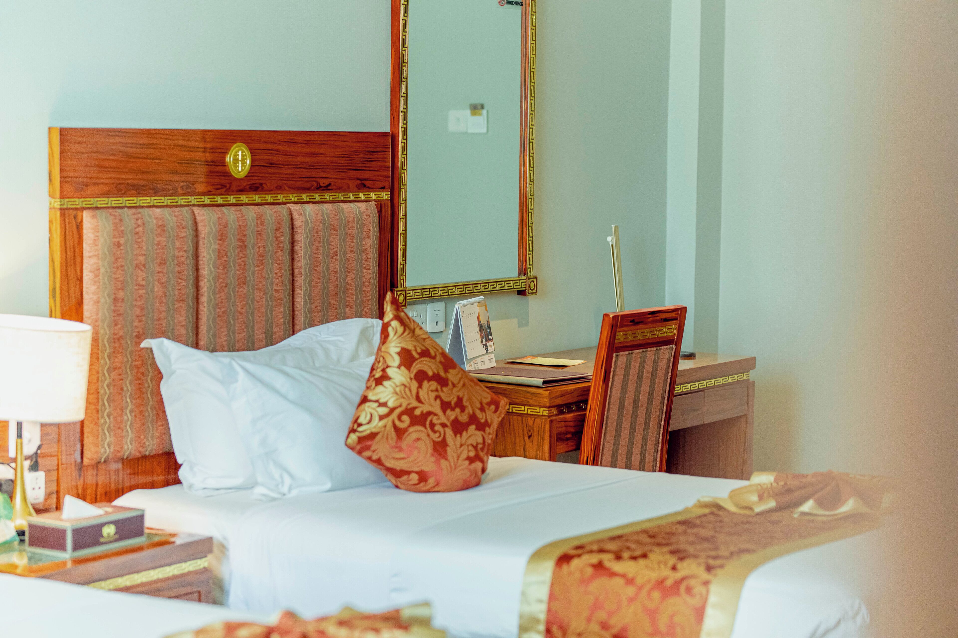 A hotel room with a bed, a desk, a chair, a lamp, and a mirror.
