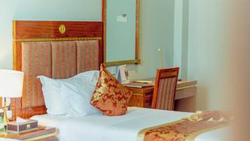 A hotel room with a bed, a desk, a chair, a lamp, and a mirror.