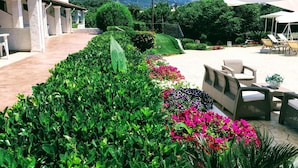A well-maintained garden with a variety of colorful flowers and neatly trimmed hedges, leading to a patio area with outdoor furniture. - Summer Wine Friendly Resort (Corfu)