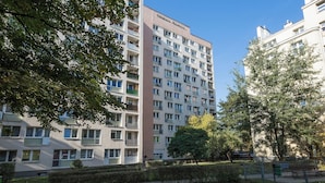 Un edificio residencial de varios pisos con balcones, un jardín cuidado y un cielo azul despejado.