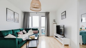 Una sala de estar moderna con un sofá verde, una mesita de centro, un televisor y un gran ventanal con cortinas.