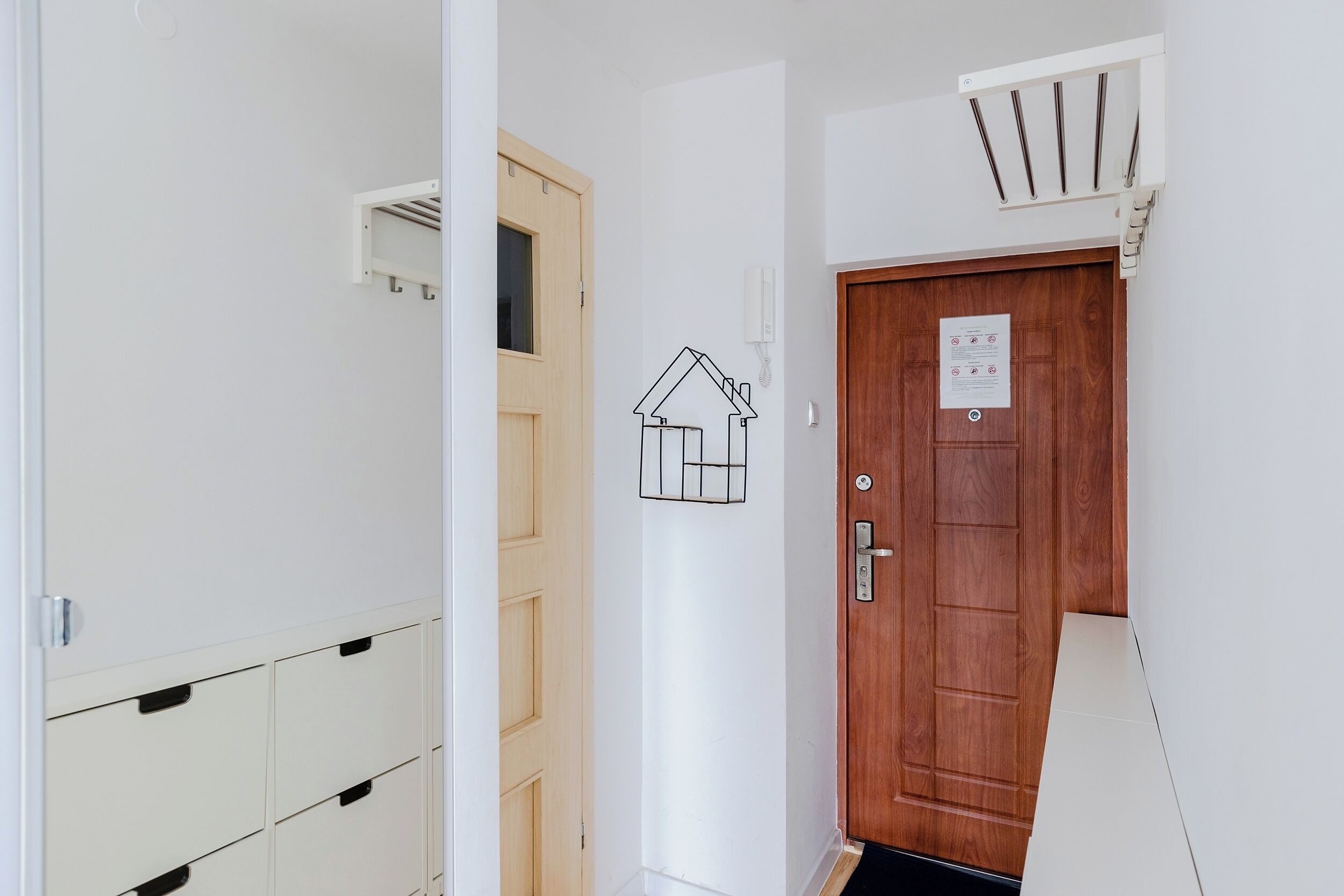 A hallway with a wooden door, a white wall with a house outline, and a white wall with a vent.