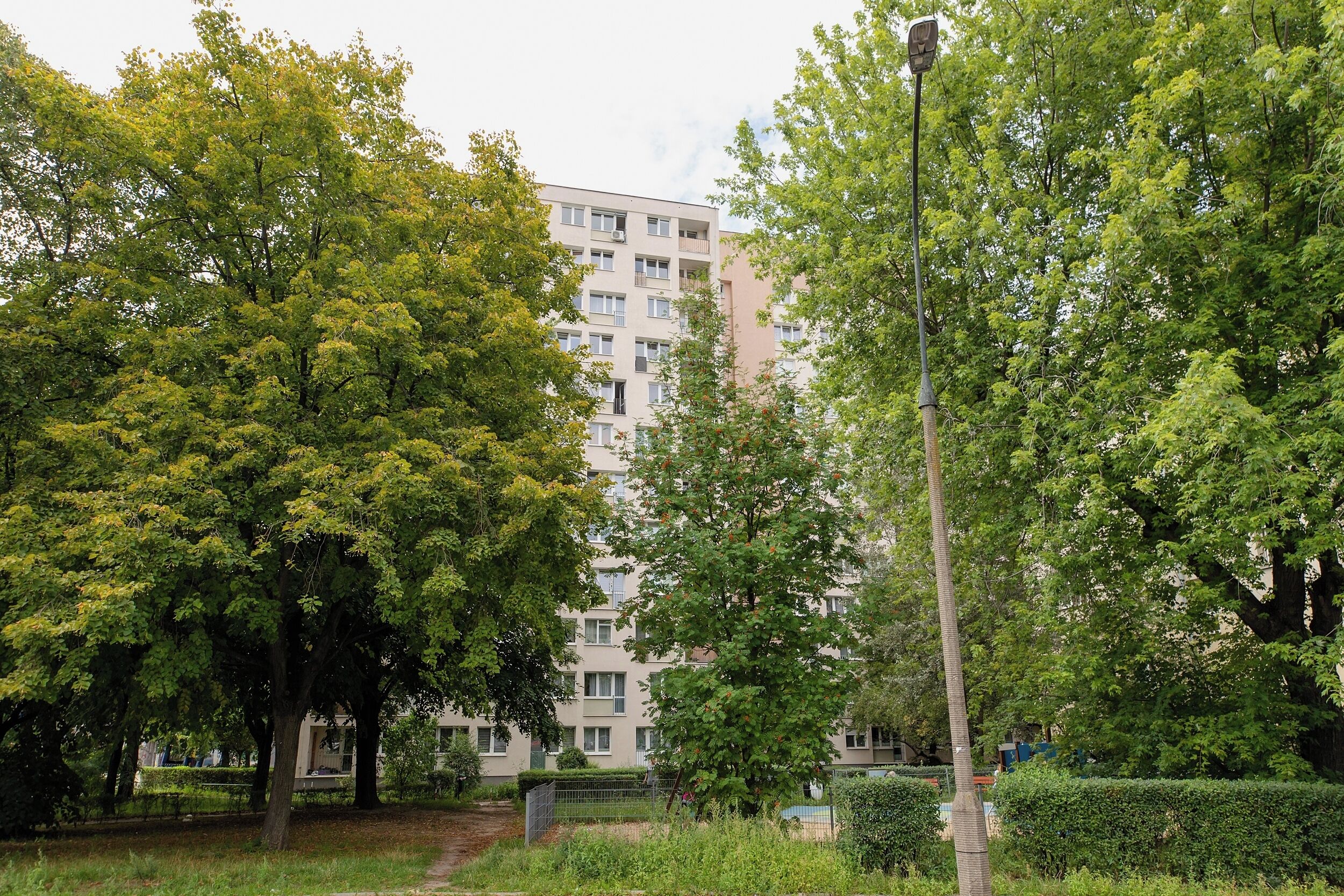 A multi-story residential building with balconies, surrounded by trees and a pathway.