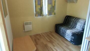 A compact room with a wooden floor, a small table, a sofa with a black and white striped cover, and a window with floral curtains.
