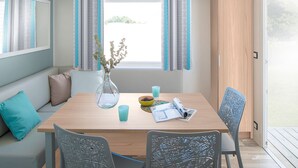 Un comedor con una mesa de madera, cuatro sillas, un florero con ramas, un cuenco de fruta y una taza.