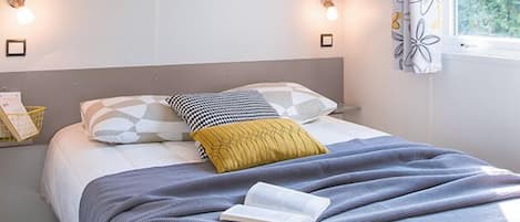 A neatly arranged bedroom with a bed, bedside lamps, and a window with curtains.