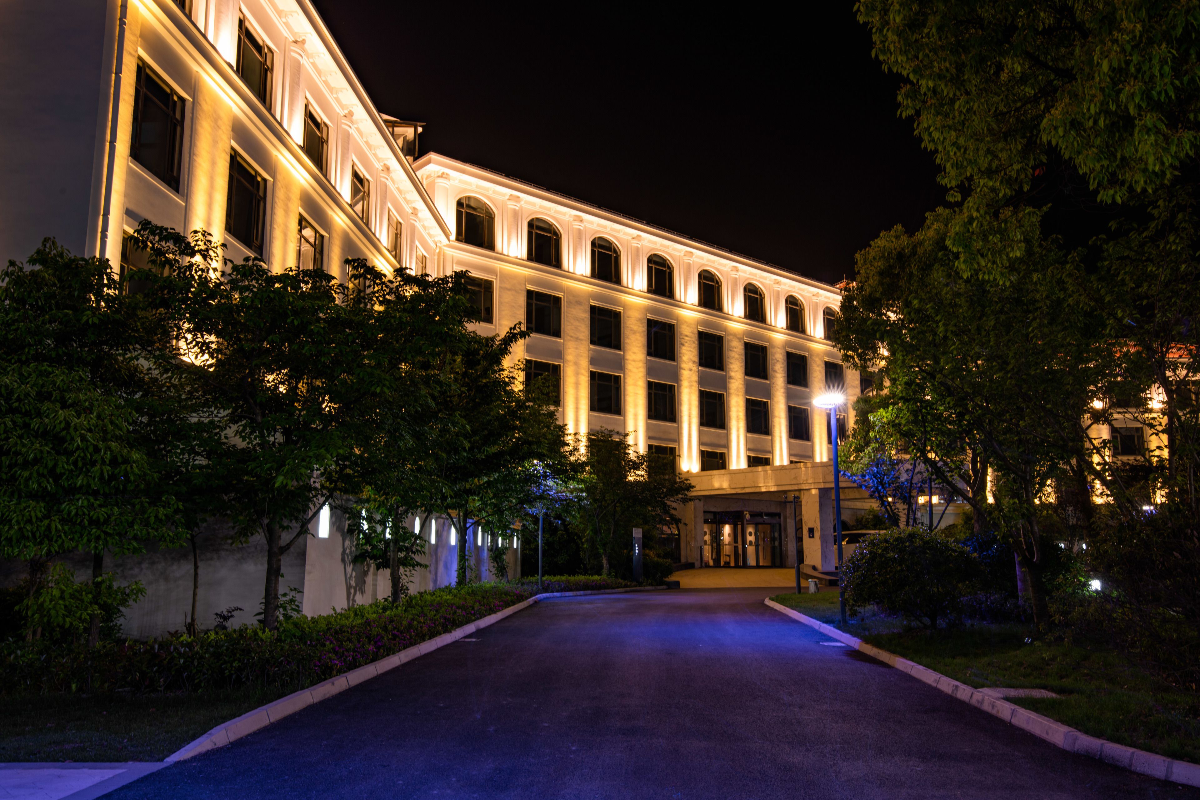 A large, well-lit building with a symmetrical facade, a central entrance, and a landscaped driveway.