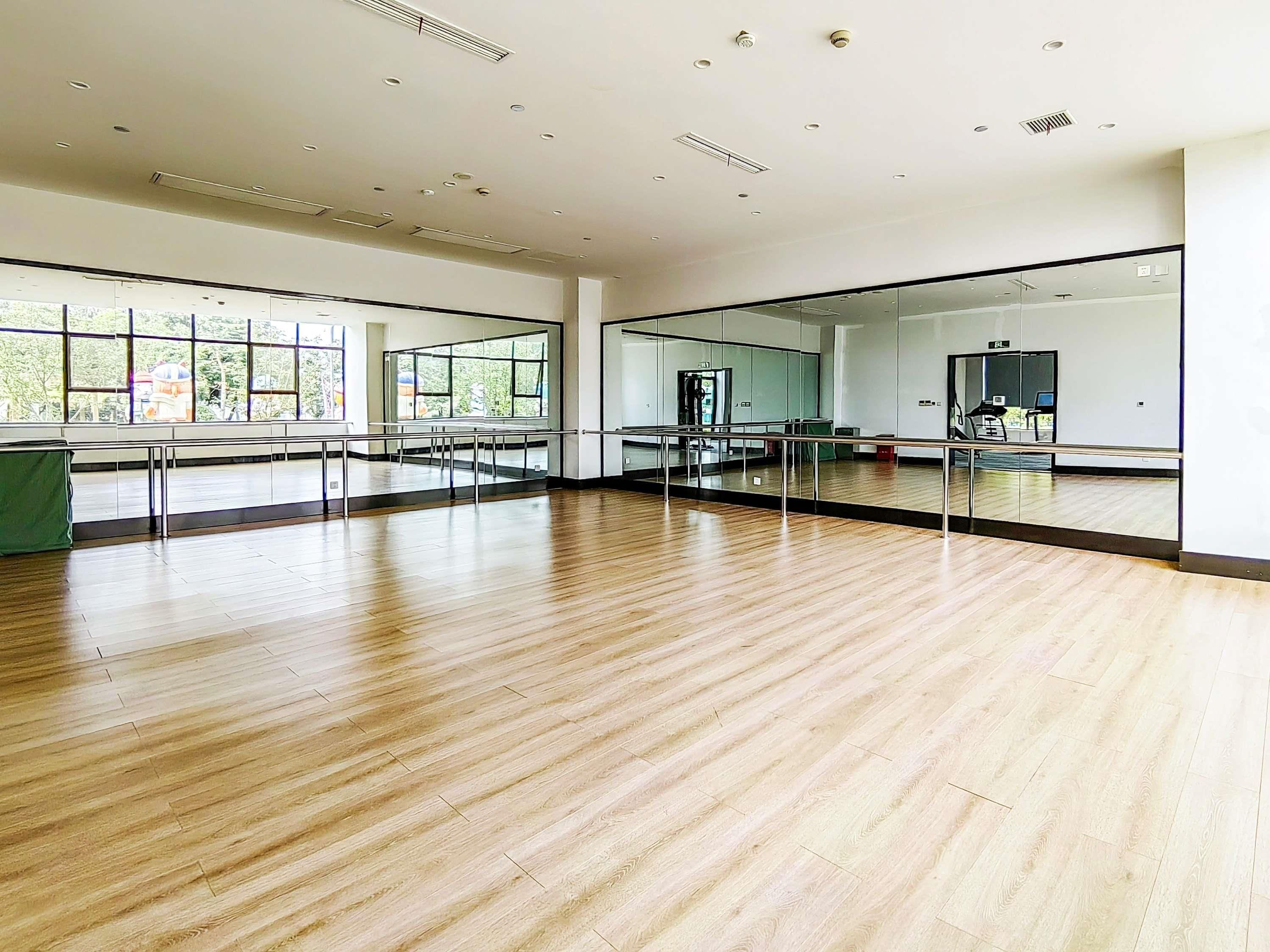 Un amplio estudio de baile con suelo de madera, ventanas grandes y espejos.