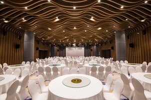A banquet hall with round tables and white chairs, a stage at the front, and a wavy ceiling design.