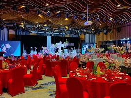 A banquet hall with round tables, red chairs, and floral centerpieces.
