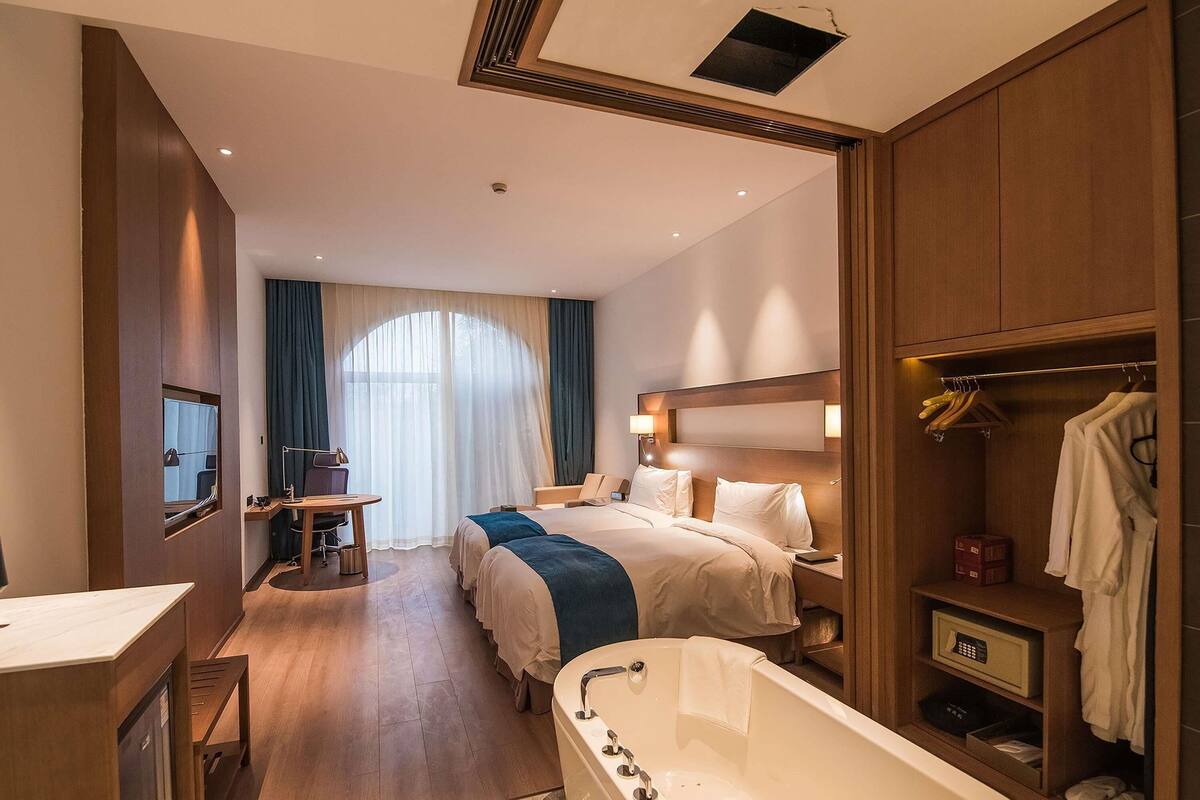 A hotel room with a large bed, a sitting area with a desk, a bathtub, and a wardrobe.