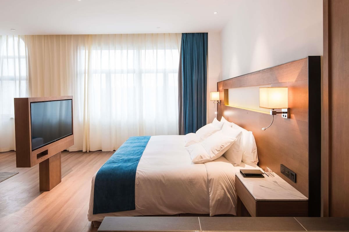 A hotel room with a bed, a TV, a bedside table, and a lamp.