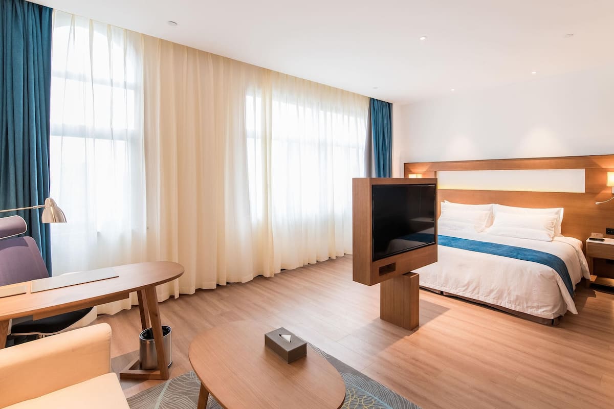 A hotel room with a bed, a desk, a chair, a TV, and a lamp.
