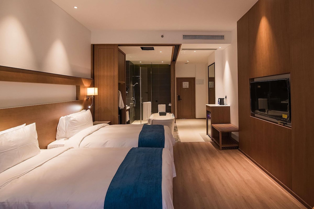 A hotel room with two beds, a shower, a vanity, and a TV.