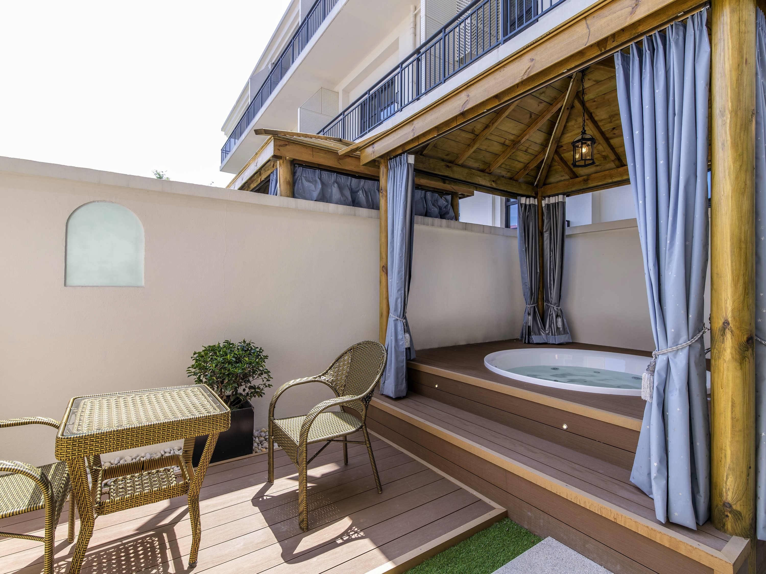 A covered outdoor seating area with wicker furniture, a small table, and a hot tub.