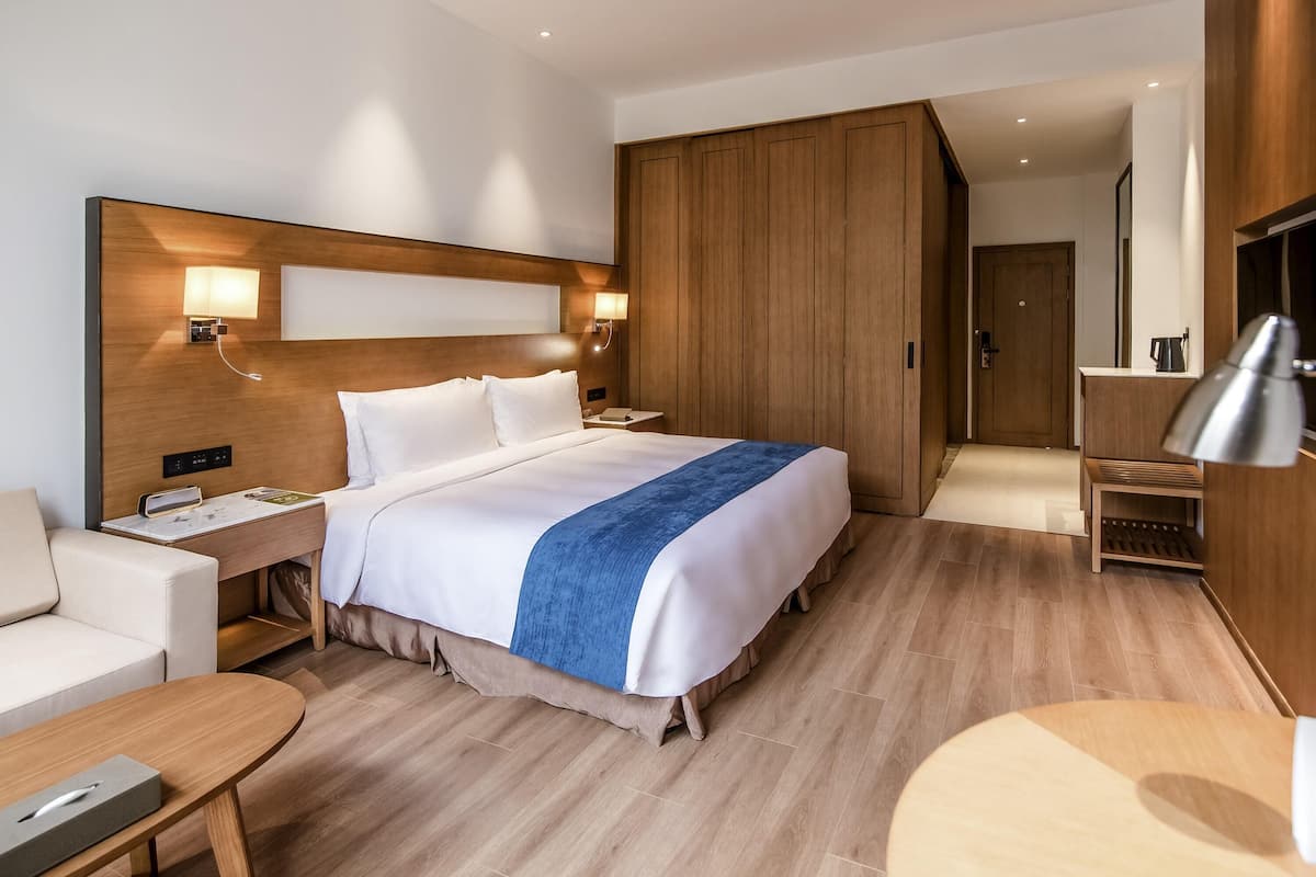 A hotel room with a large bed, bedside tables, a desk, a wardrobe, and a TV.