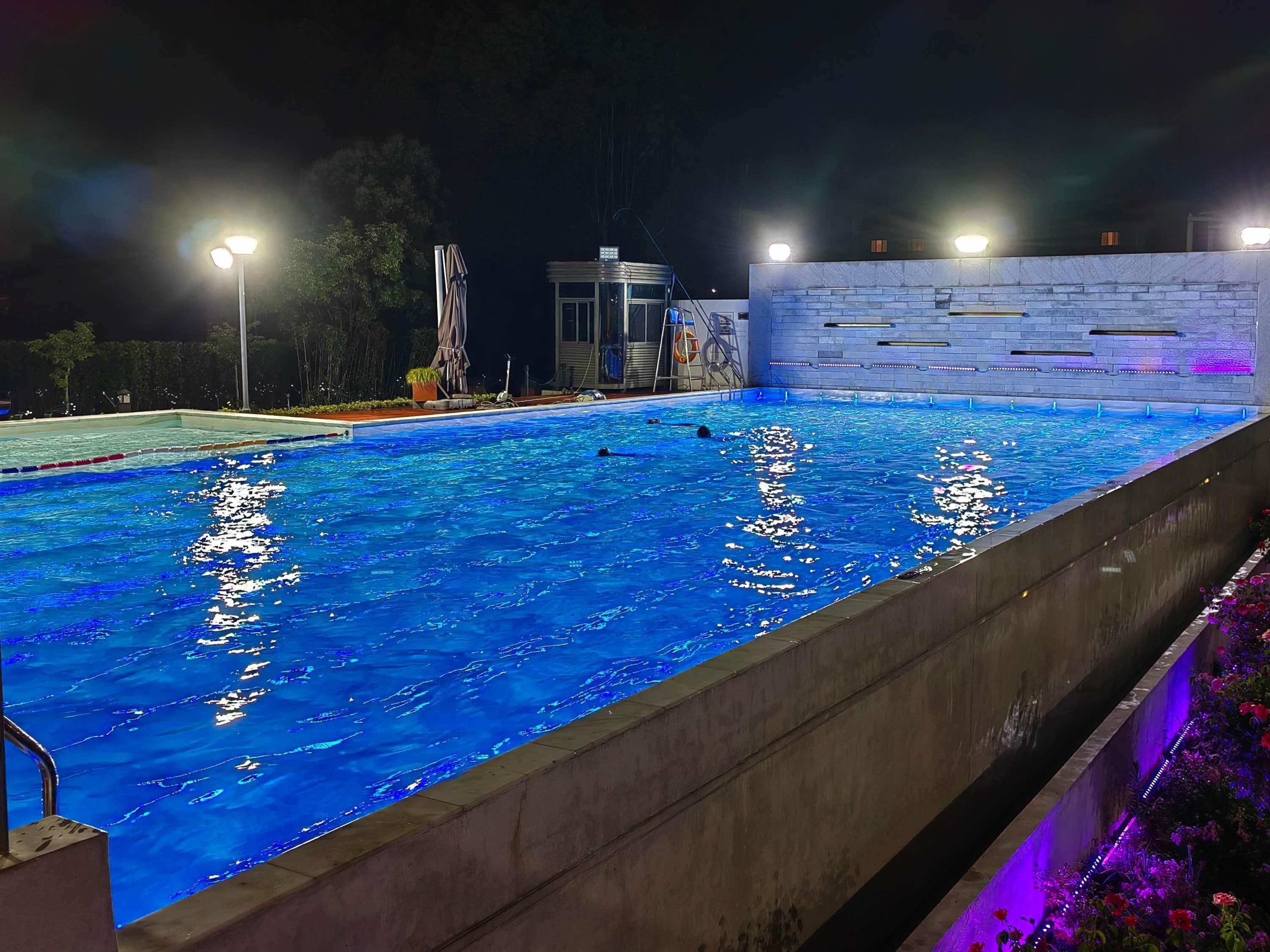 A swimming pool at night with clear water, surrounded by a concrete wall and a stone facade.