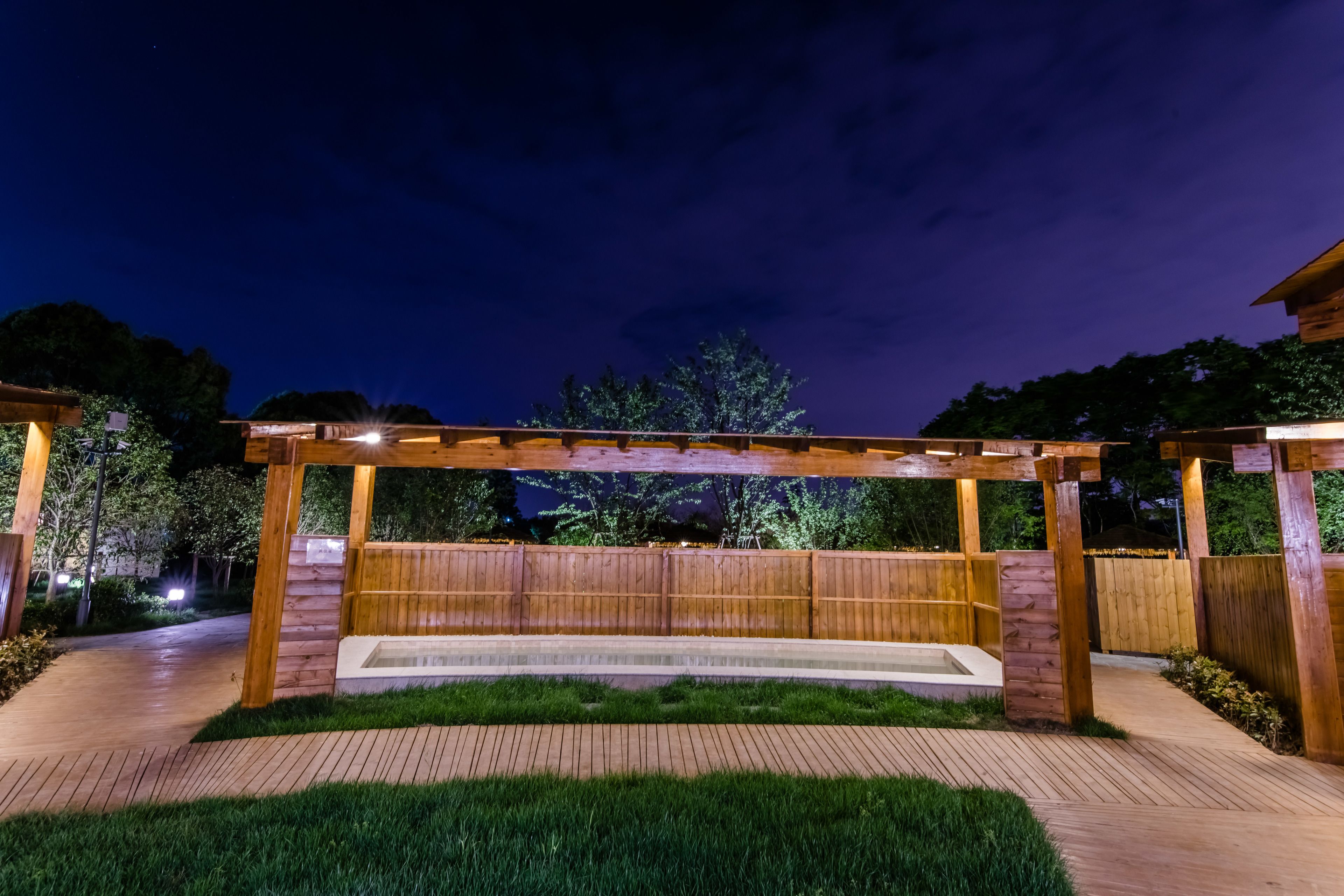 A wooden pergola structure with a built-in bench and a small water feature.