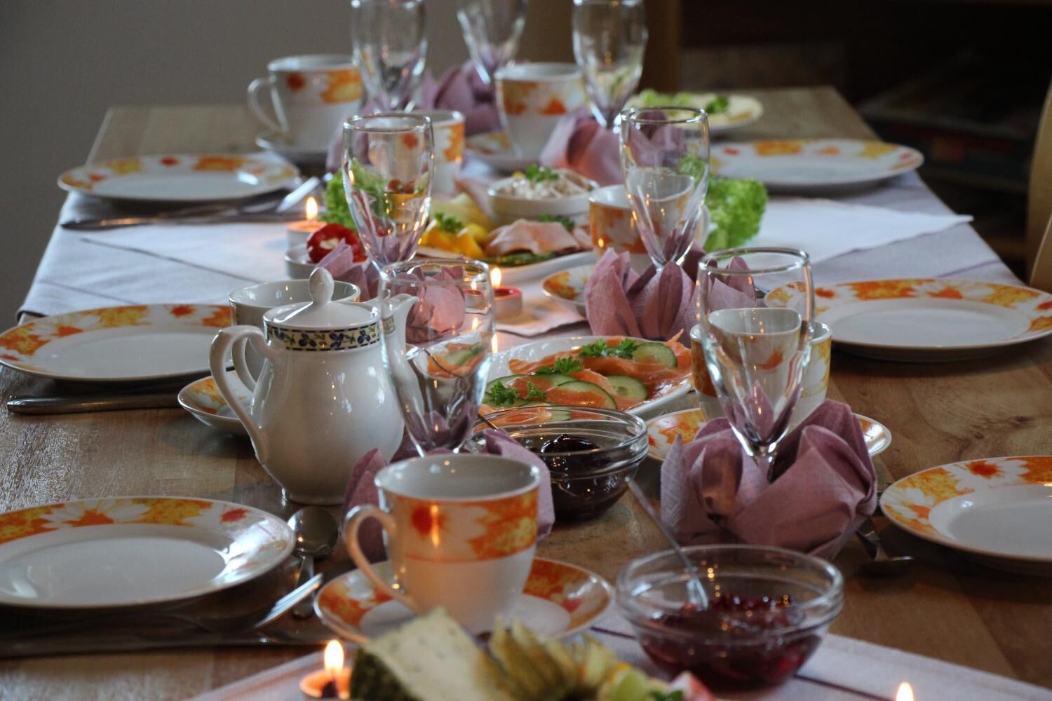 A dining table set with plates, glasses, a pitcher, and candles, suggesting a formal meal setting.