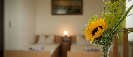 Una habitación con cama, mesita de noche y un jarrón con flores sobre una mesa.