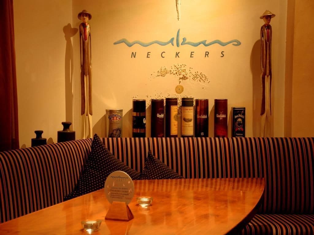 A restaurant interior with a wooden table, striped upholstered seating, and a wall displaying various bottles and a logo.