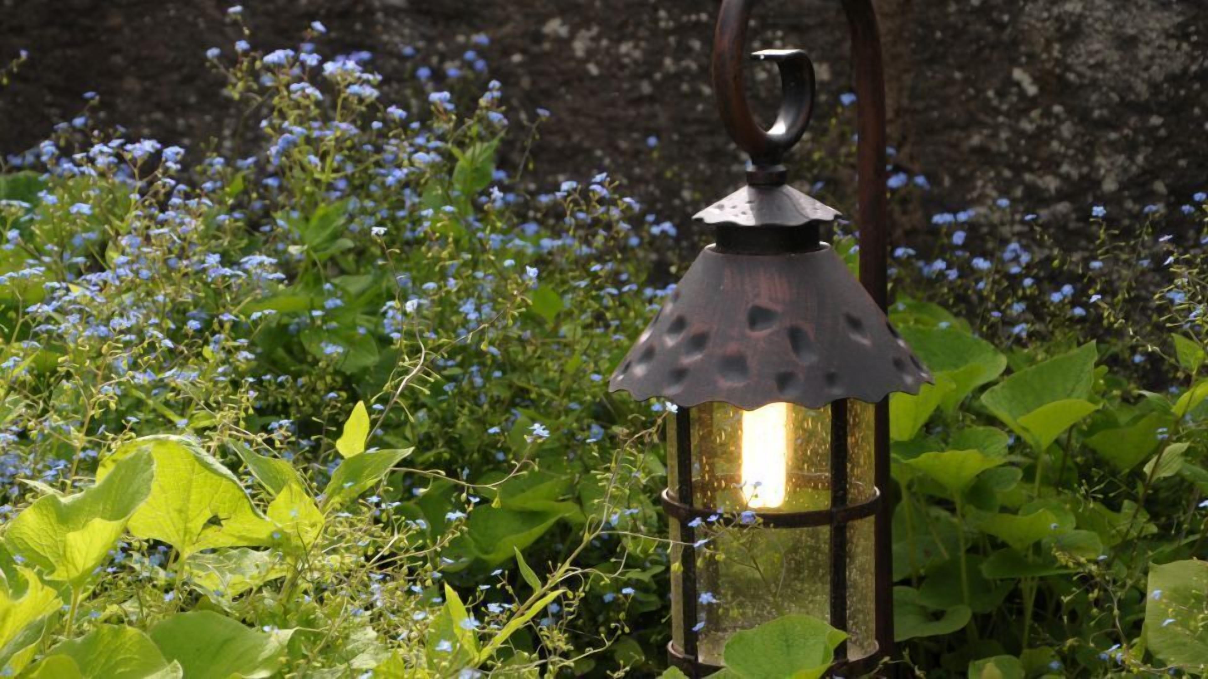 Un farol en un jardín con flores azules y follaje verde.