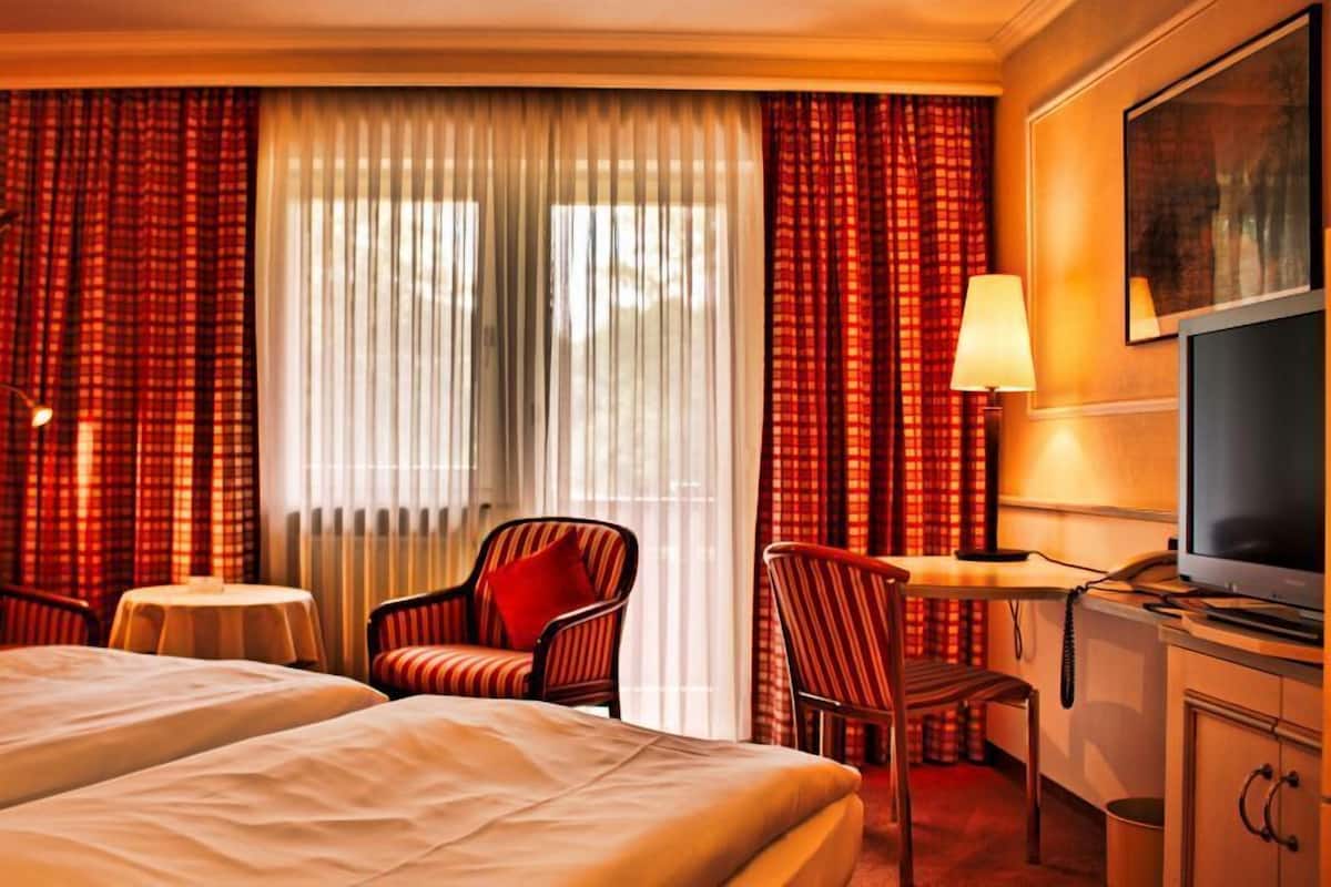 Ein Hotelzimmer mit zwei Betten, einem Schreibtisch mit Lampe, einem Fernseher und einem Sessel.