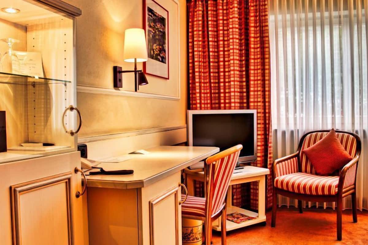 Ein Hotelzimmer mit Schreibtisch, Stuhl, Fernseher und einem Fenster mit Vorhängen.