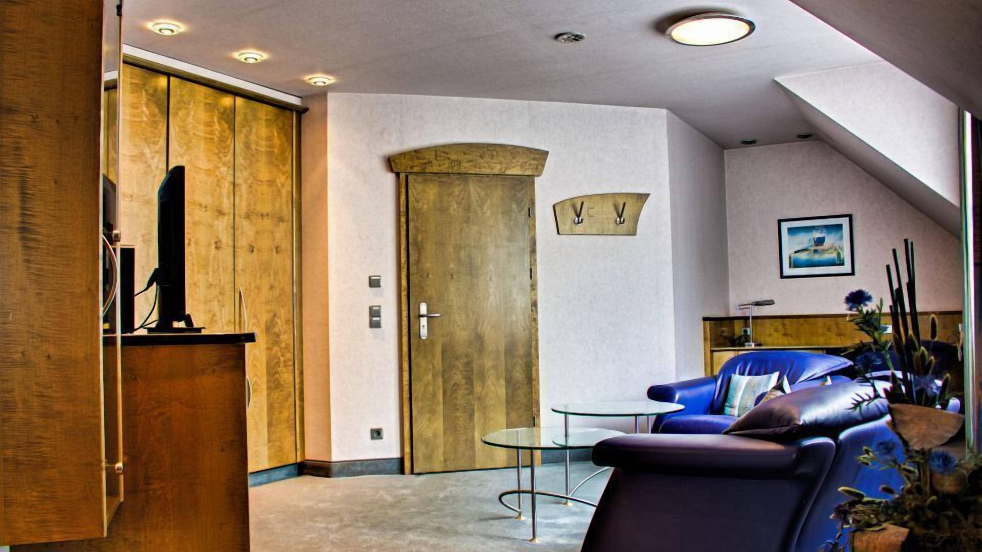 Ein modernes Interieur mit einer Holztür, einem blauen Ledersofa, einem Glastisch und einem gerahmten Bild an der Wand.