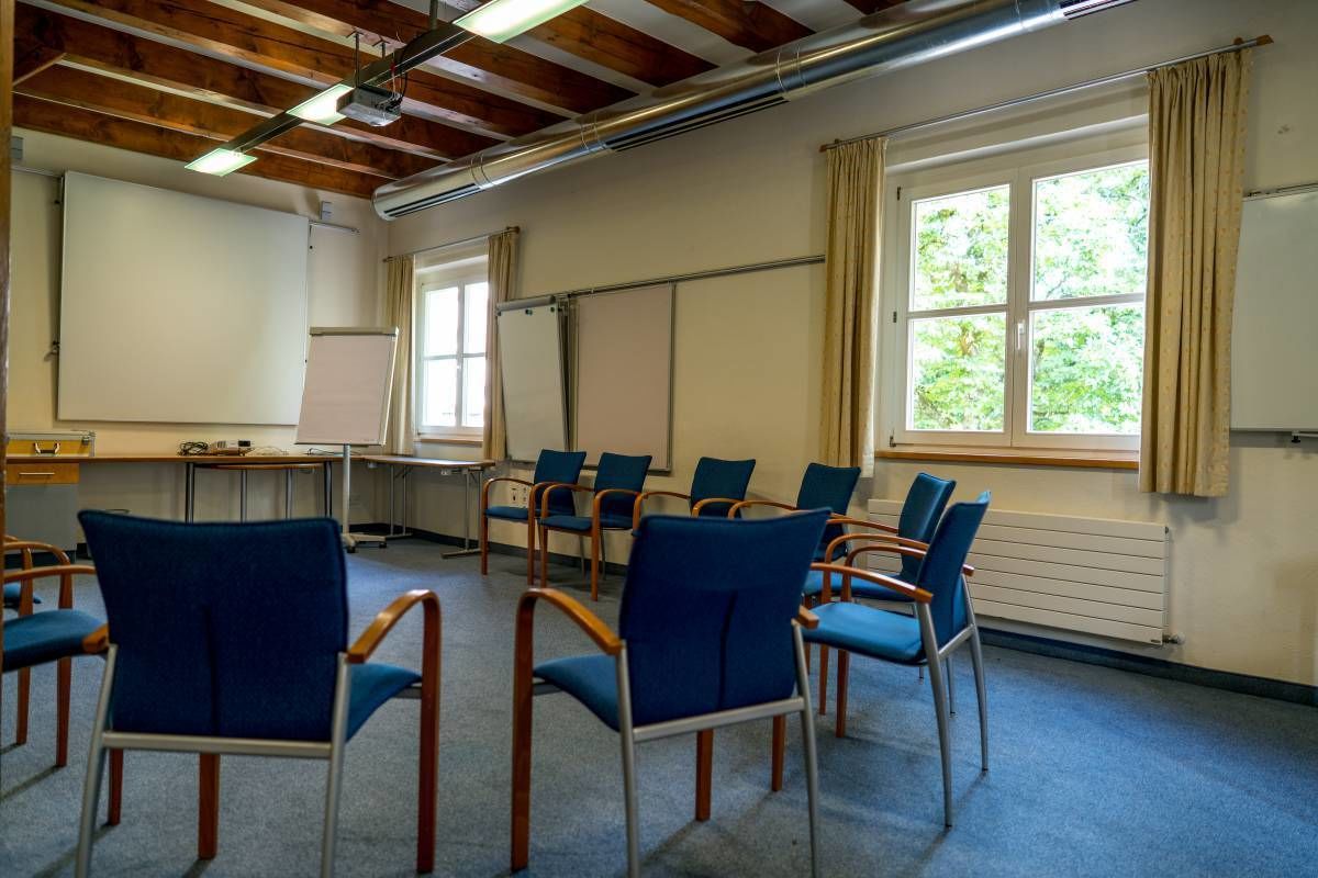 A conference room with blue chairs, a whiteboard, and a large window with curtains.