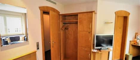 A room with a wooden wardrobe, a television on a stand, and a window with a view.
