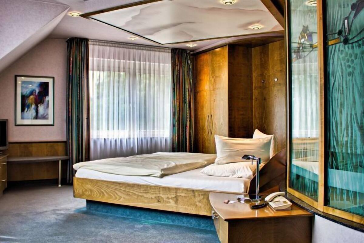 Ein modernes Hotelzimmer mit einem großen Bett, einem Schreibtisch, einem Fernseher und einem großen Fenster mit Vorhängen.