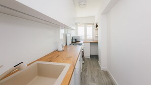 A narrow kitchen with a wooden countertop, white appliances, and a window providing natural light. - ShortStayPoland Aleja Solidarności - B61 (Warsaw)