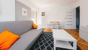 A modern living room with a grey sofa, orange pillows, a white coffee table, and a patterned rug. - ShortStayPoland Aleja Solidarności - B61 (Warsaw)