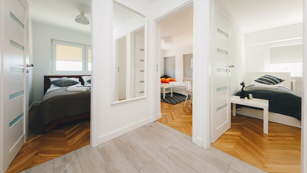 A modern bedroom with a bed, bedside table, and a desk with a chair. There is a door leading to another room. - ShortStayPoland Aleja Solidarności - B61 (Warsaw)