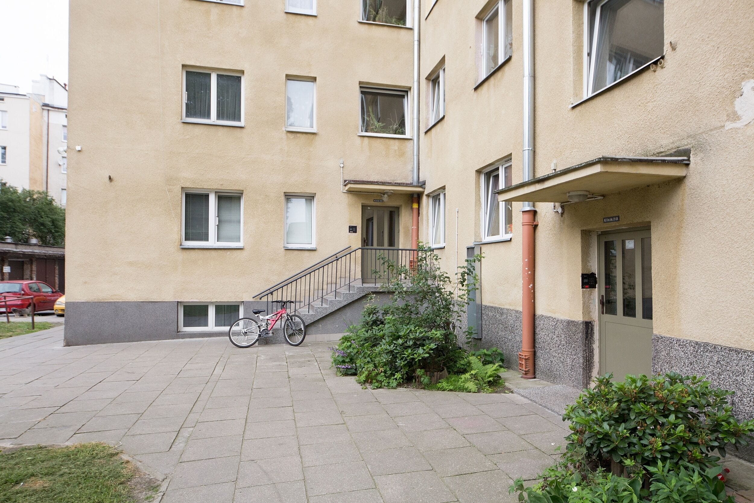 Un edificio de varios pisos con fachada plana, una escalera que conduce a la entrada y una bicicleta estacionada afuera.