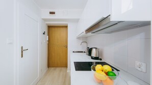 A modern kitchen with white cabinetry, a wooden door, a black countertop, and a bowl of fruit. - ShortStayPoland Grottgera B198 (Warsaw)