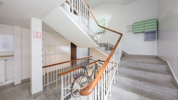 A staircase with a wooden handrail, a bicycle parked at the bottom, and a bulletin board with green and gray folders. - ShortStayPoland Grottgera B198 (Warsaw)