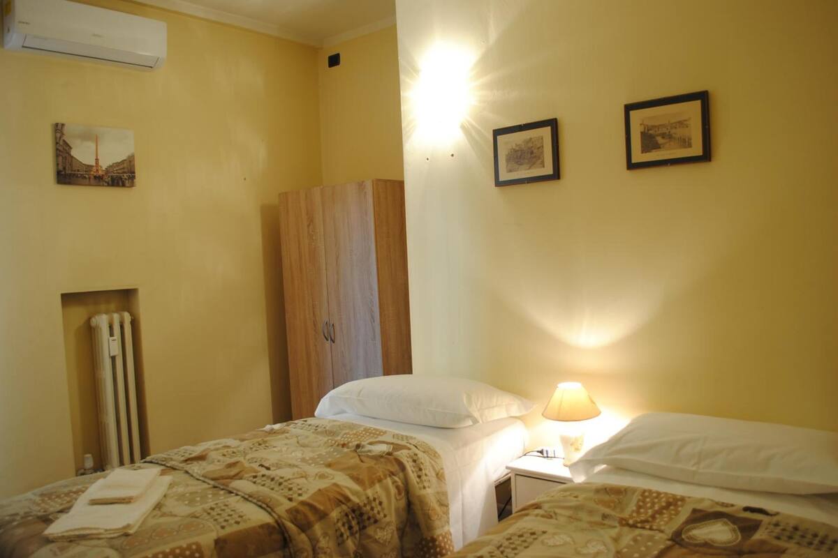 Een hotelkamer met twee bedden, een houten garderobe, een radiator en foto's aan de muur.